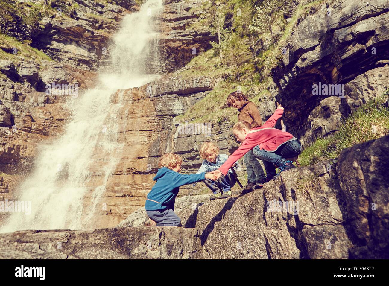 Gruppo di bambini arrampicata roccia accanto a cascata Foto Stock