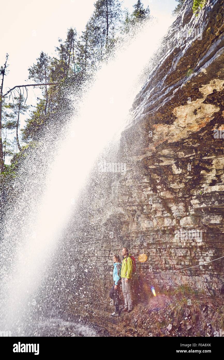 Coppia giovane piedi sotto la cascata, guardando fuori, Tirolo, Austria Foto Stock