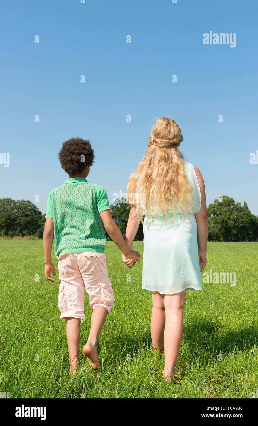Vista posteriore del ragazzo e una ragazza passeggiano mano nella mano nel campo Foto Stock