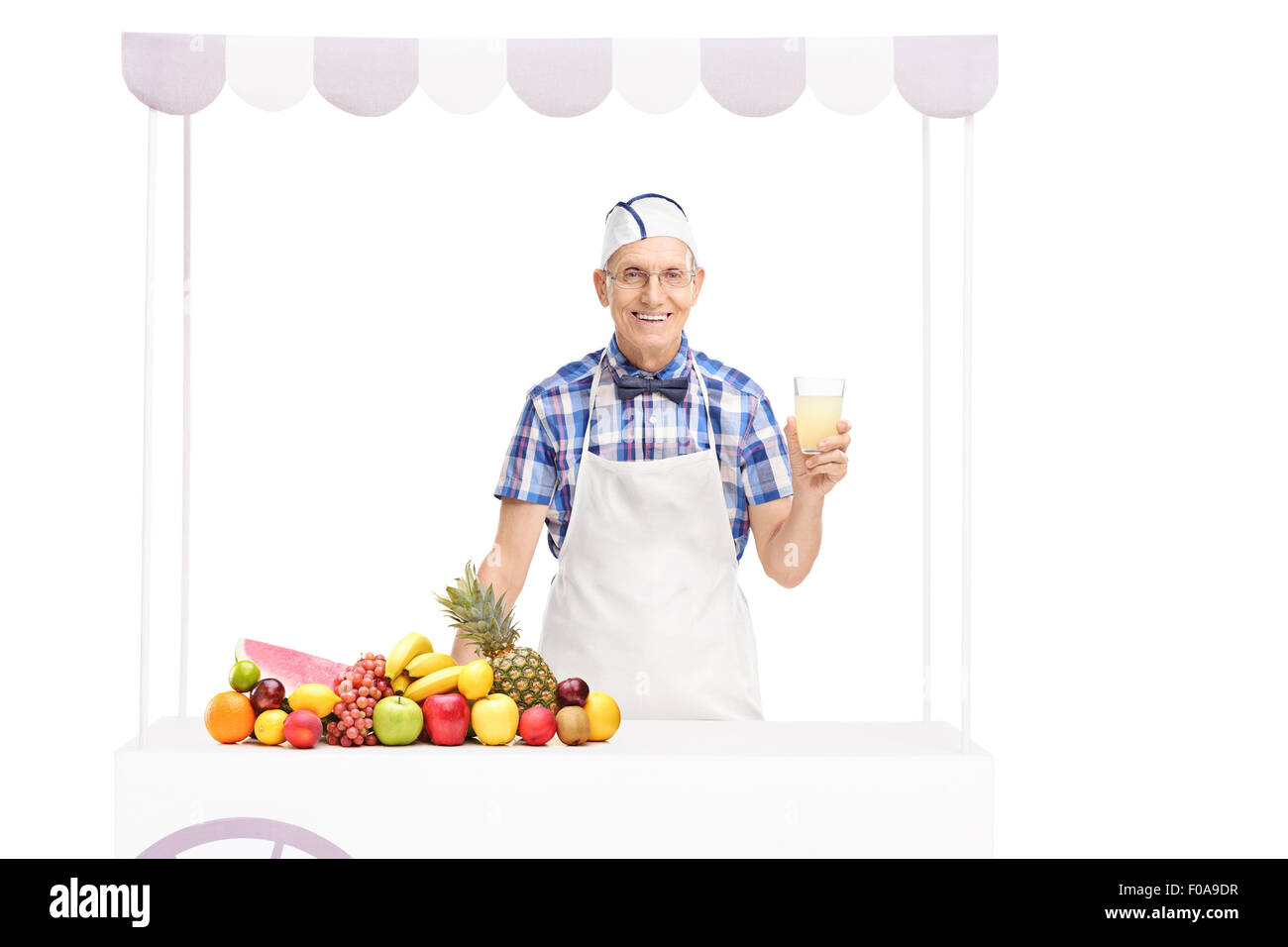 Senior soda jerk tenendo un bicchiere di limonata e di stare dietro a una fase di stallo con un mucchio di frutti su di esso Foto Stock