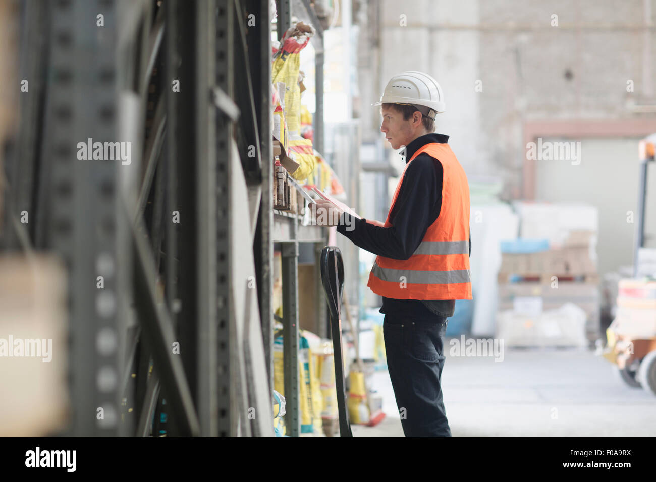 Giovane maschio lavoratore magazzino ricerca ripiani con appunti in magazzino Foto Stock