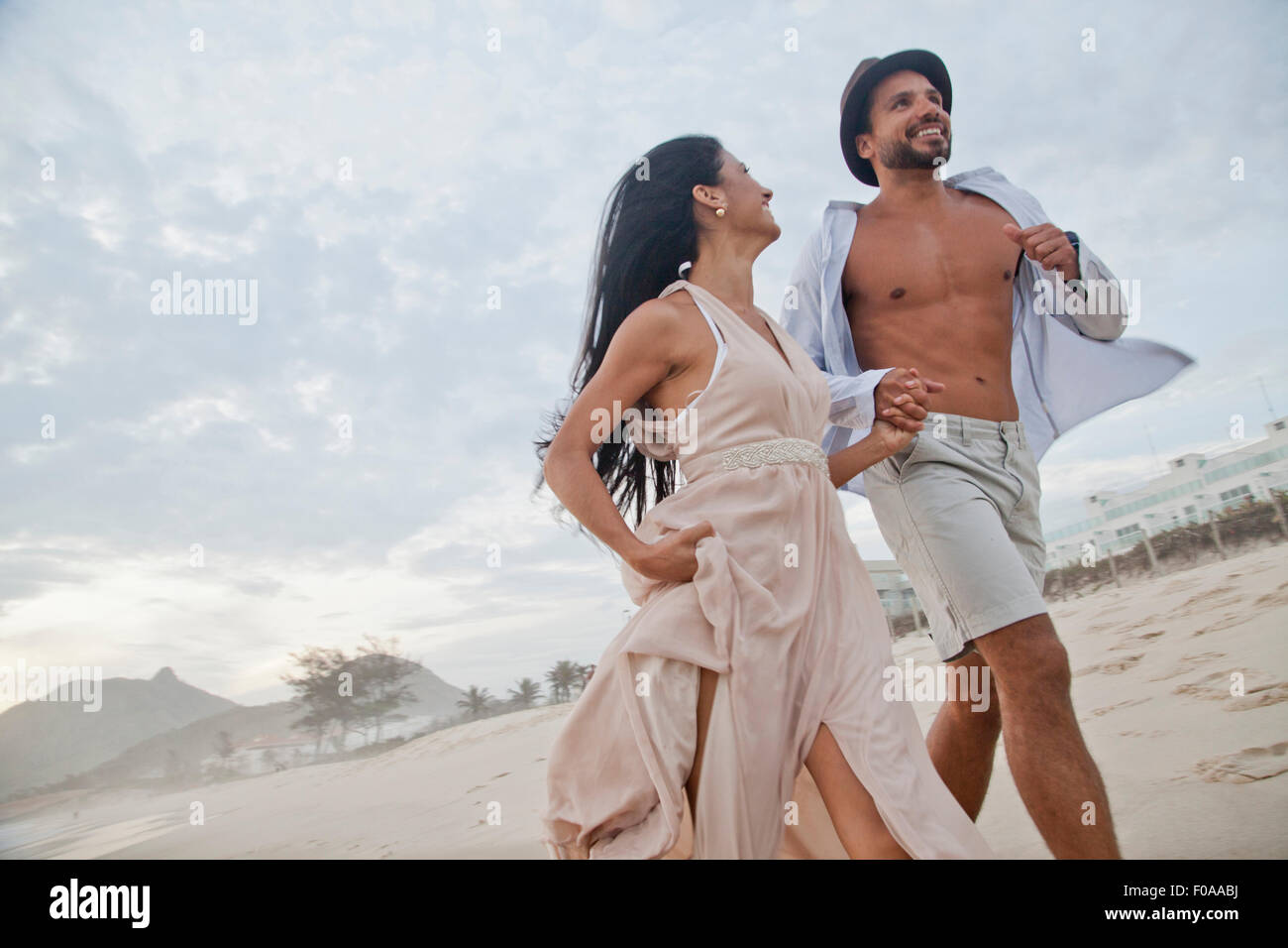 Metà adulto giovane che corre lungo la spiaggia, mano nella mano, basso angolo di visione Foto Stock