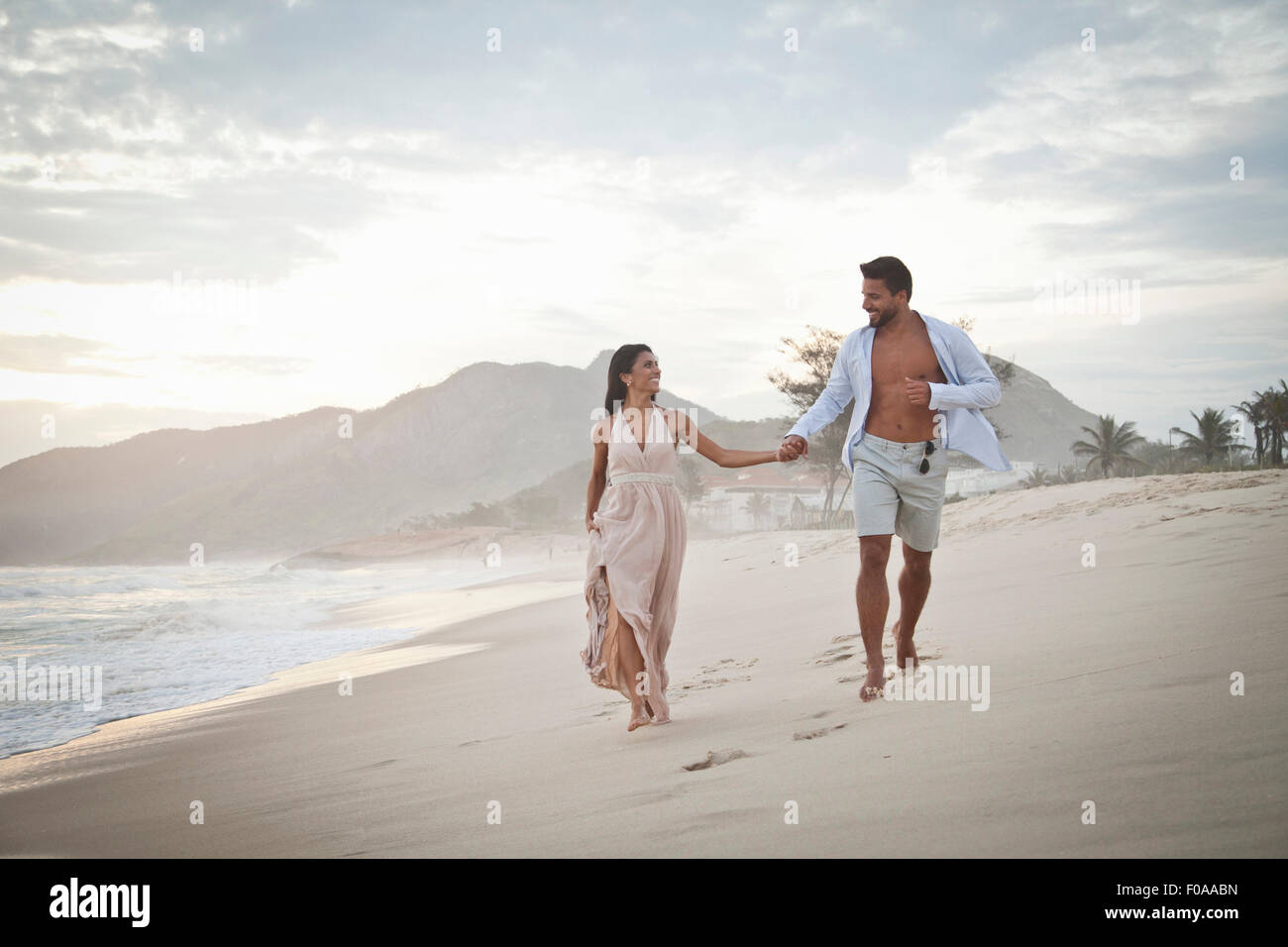 Metà adulto giovane camminando lungo la spiaggia, mano nella mano Foto Stock