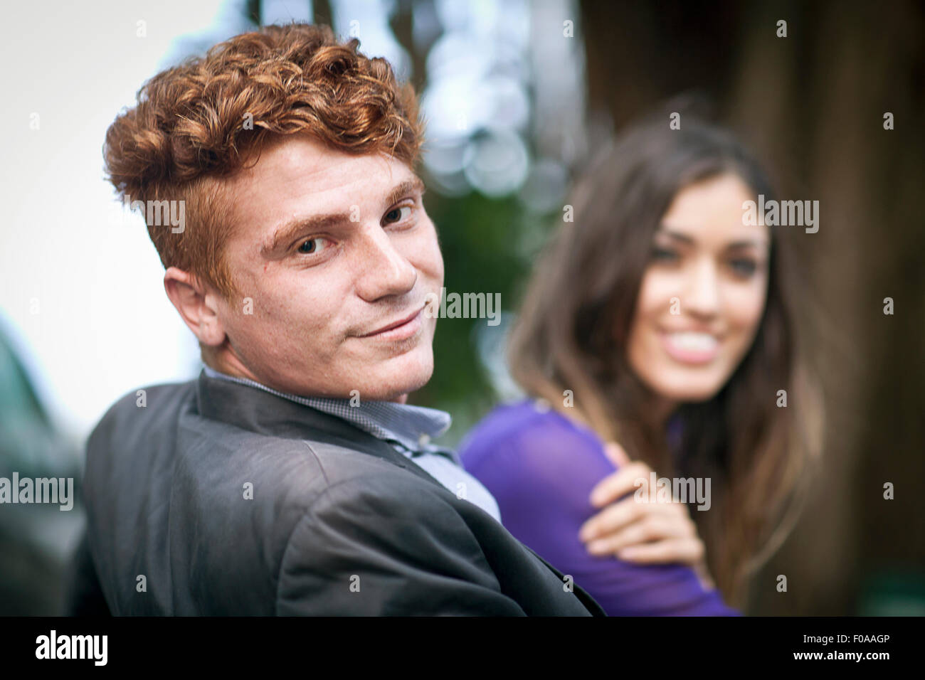 Coppia giovane seduti insieme, all'aperto, guardando la telecamera, sorridente Foto Stock