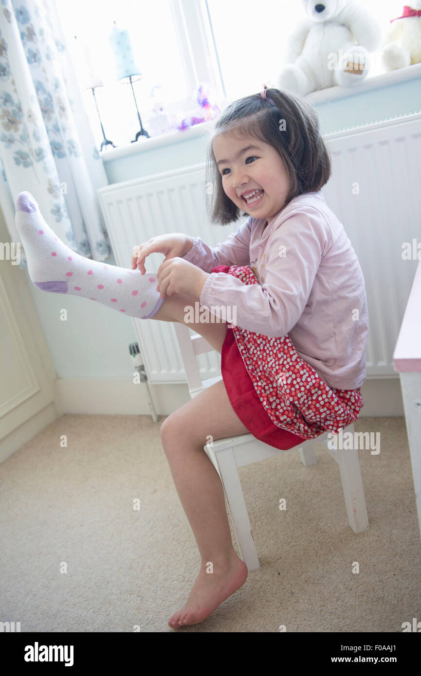 Giovane ragazza seduta sulla sedia, tirando il calzino su Foto Stock