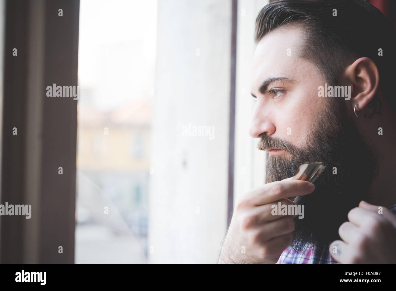Giovane uomo barbuto rifilatura della sua barba da finestra Foto Stock