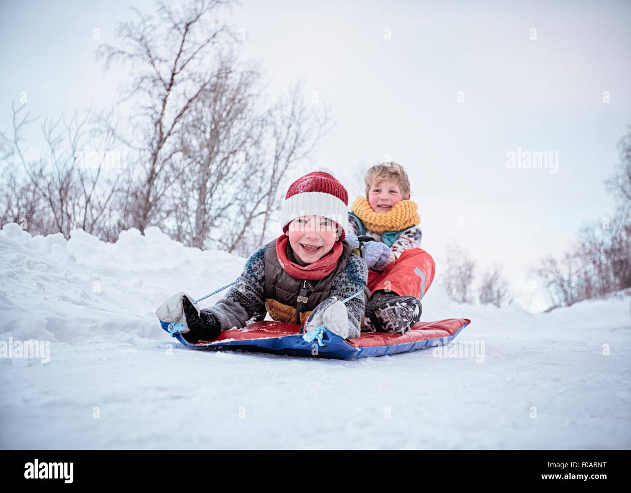 Basso angolo vista di due fratelli sul toboga sulla coperta di neve hill, Hemavan,Svezia Foto Stock