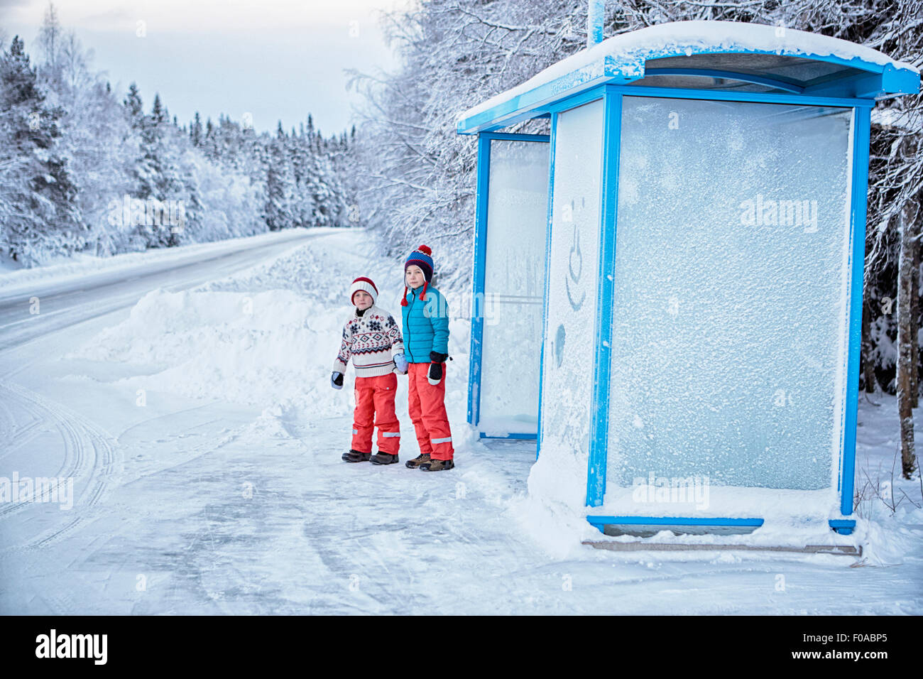 Due fratelli in attesa in coperta di neve fermata bus, Hemavan,Svezia Foto Stock