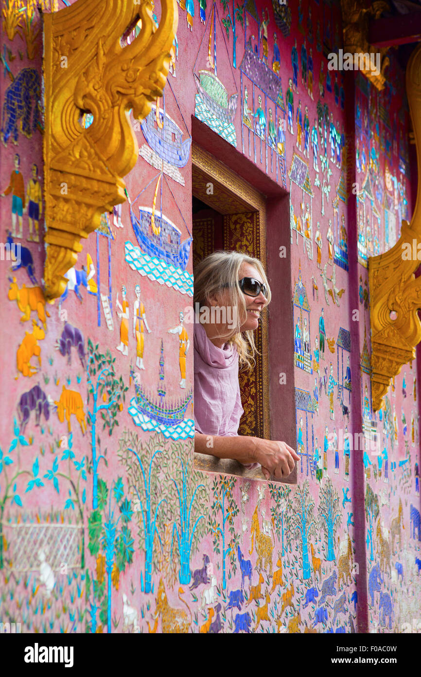 Turista femminile guardando fuori di Wat Xieng Thong finestra, Luang Prabang, Laos Foto Stock