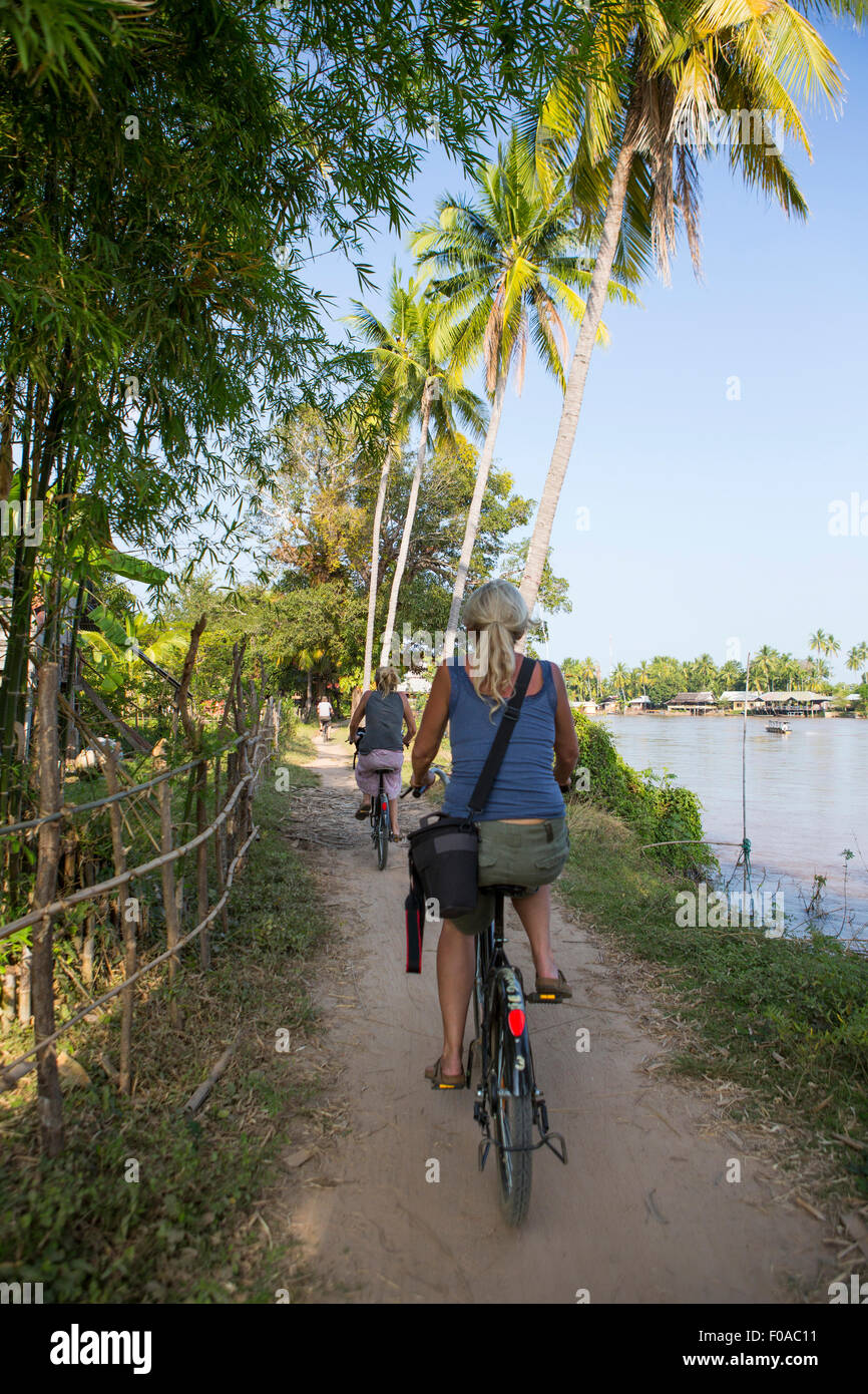 Vista posteriore di due femmina turisti in bicicletta sulla riva del Mekong, Don Det, Laos Foto Stock