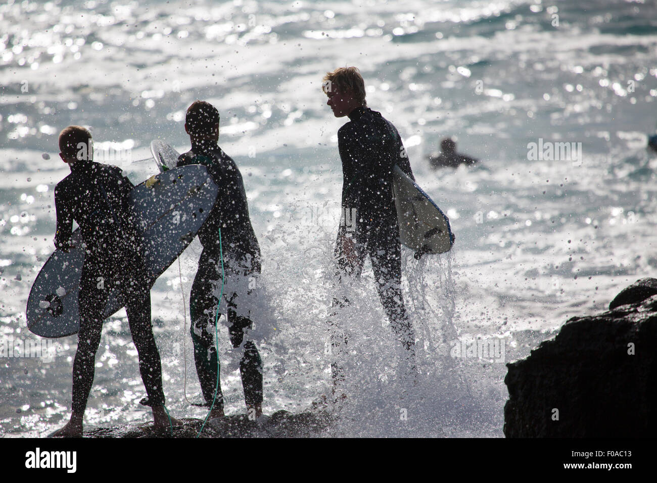 Tre stagliano surfisti maschio in piedi sul mare rocce, Fuerteventura, Spagna Foto Stock