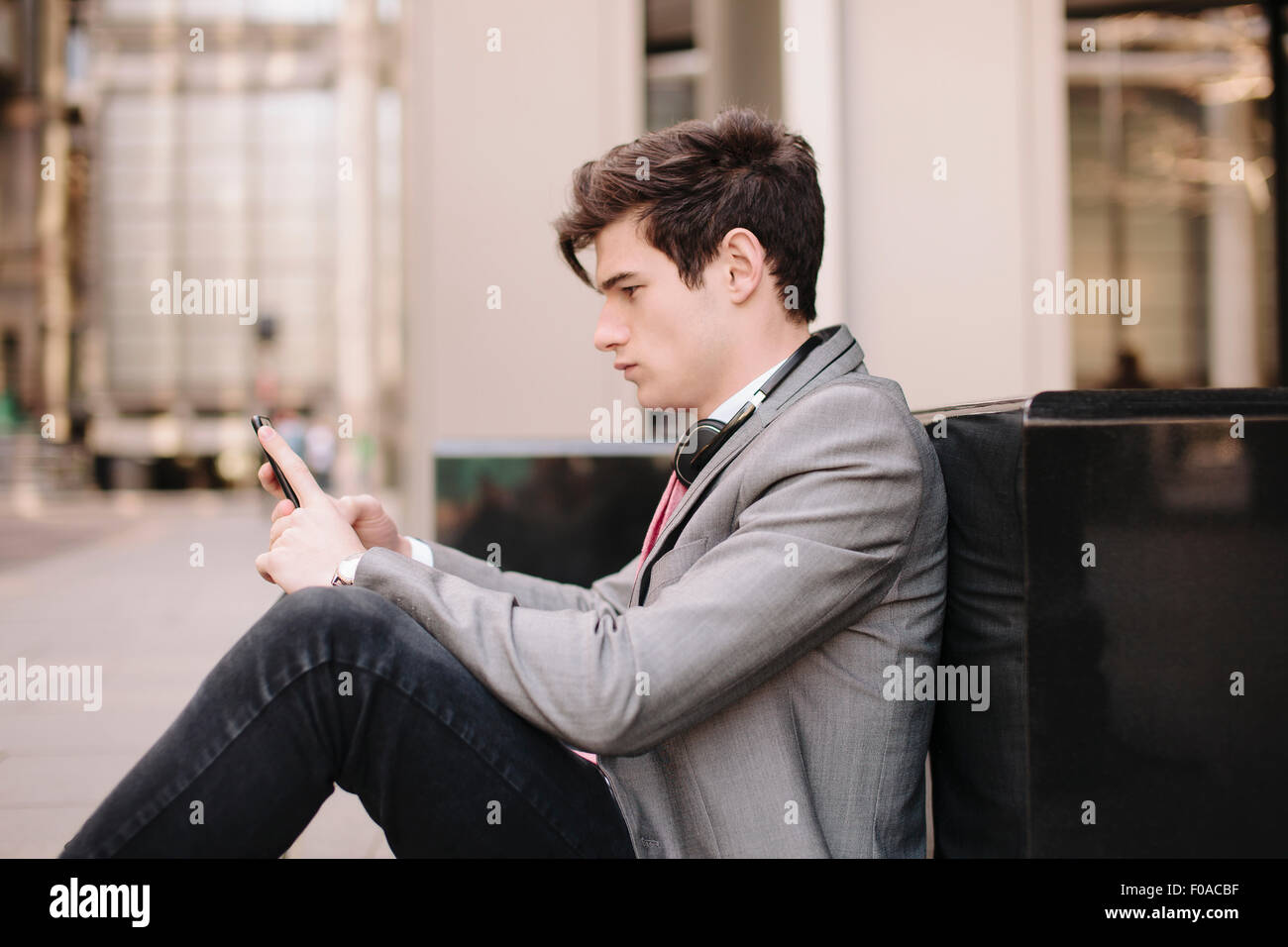 Città giovane imprenditore seduto sul marciapiede di lettura dei messaggi dello smartphone Foto Stock