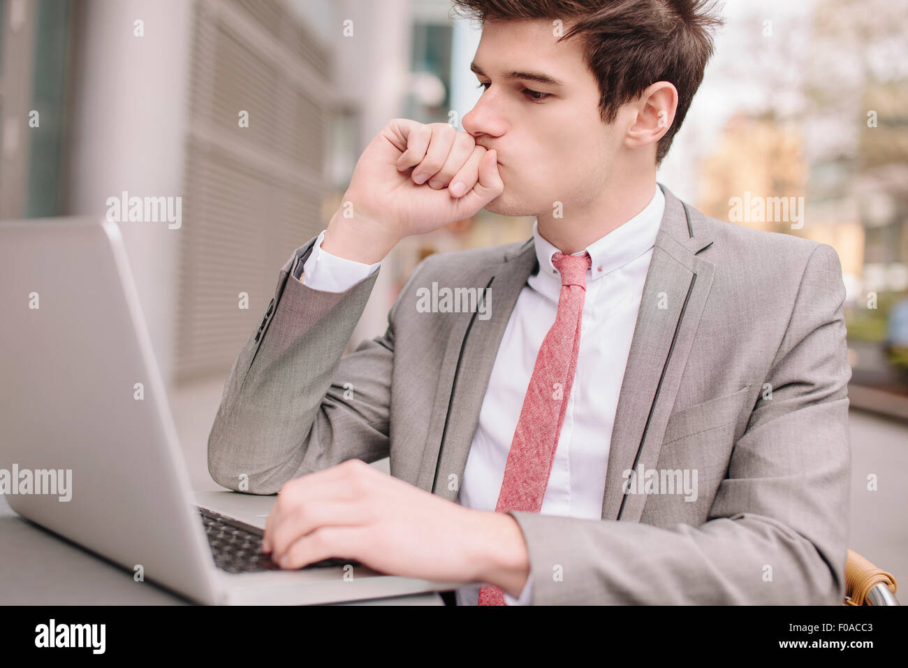 Preoccupato per il giovane imprenditore città utilizzando computer portatile presso cafè sul marciapiede Foto Stock