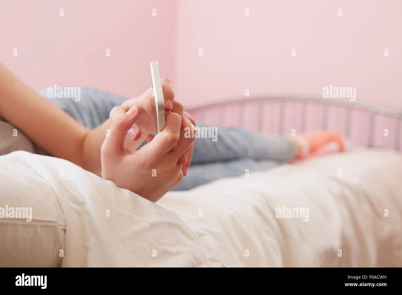 Vista ritagliata della ragazza distesa sul letto dello smartphone di lettura dei messaggi di testo Foto Stock