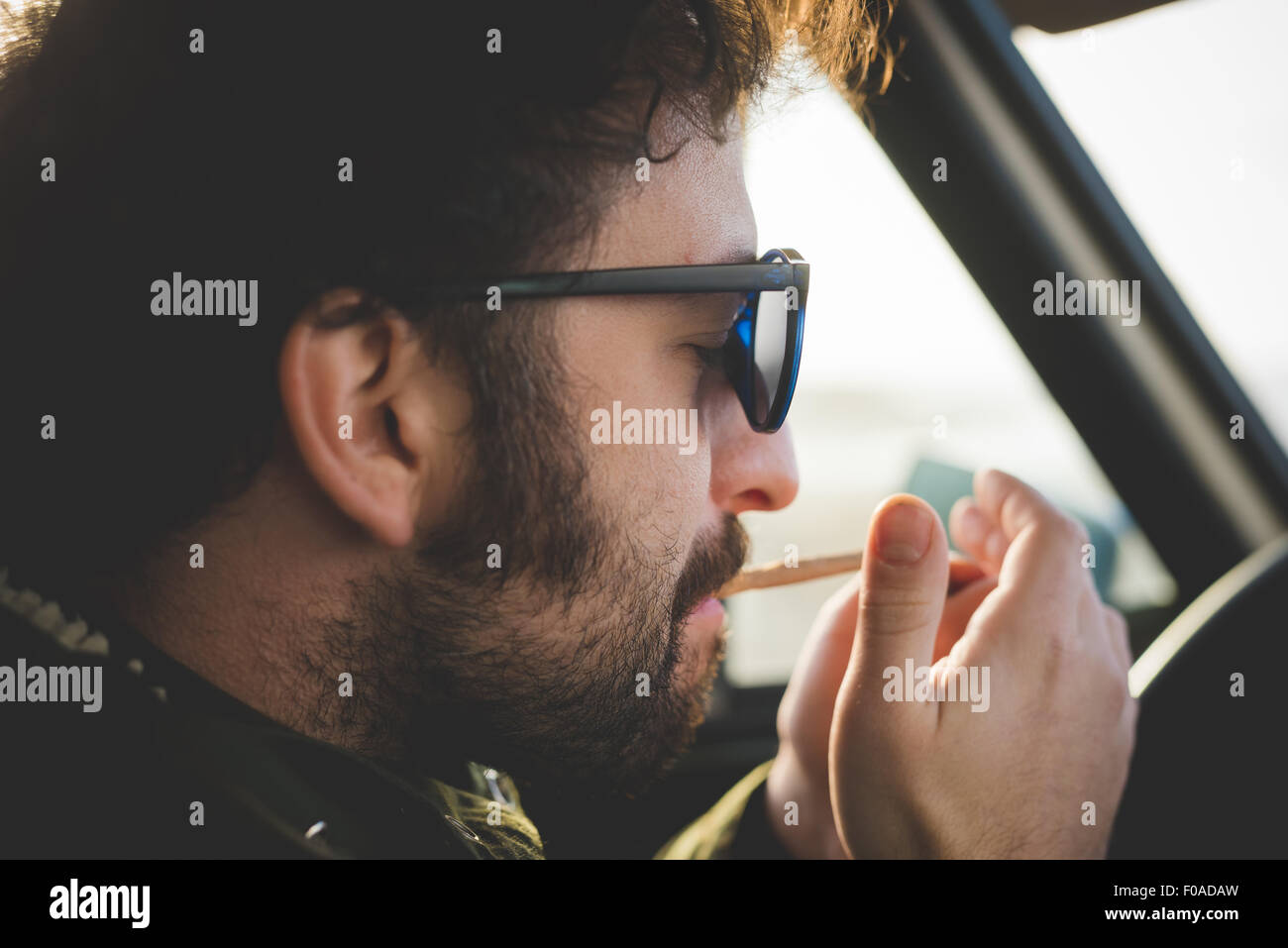 In prossimità di metà uomo adulto in auto accendere una sigaretta Foto Stock