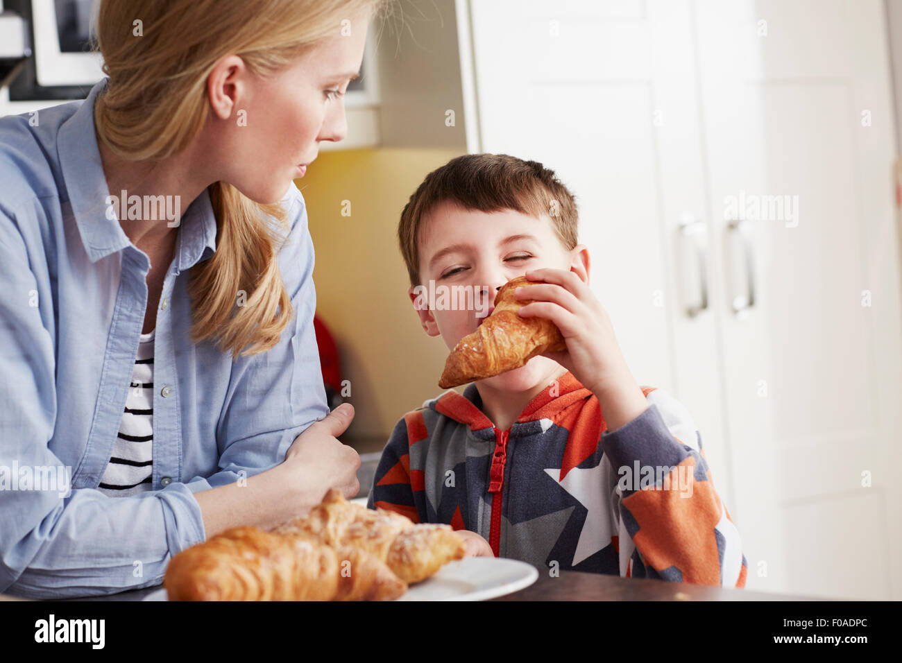Ragazzo di mordere il croissant, madre guardando Foto Stock
