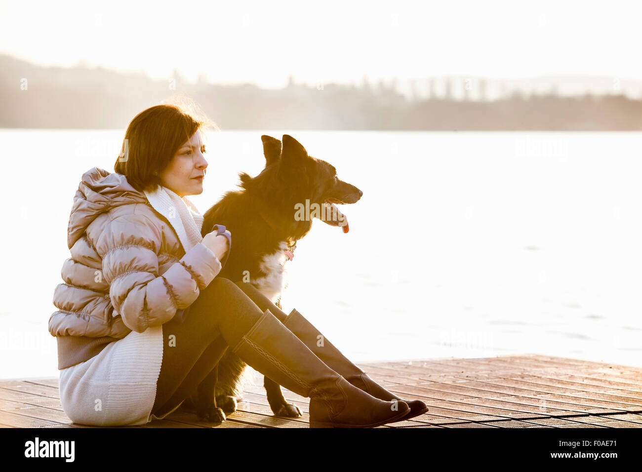Metà donna adulta e il suo cane seduto sul lago soleggiato pier Foto Stock