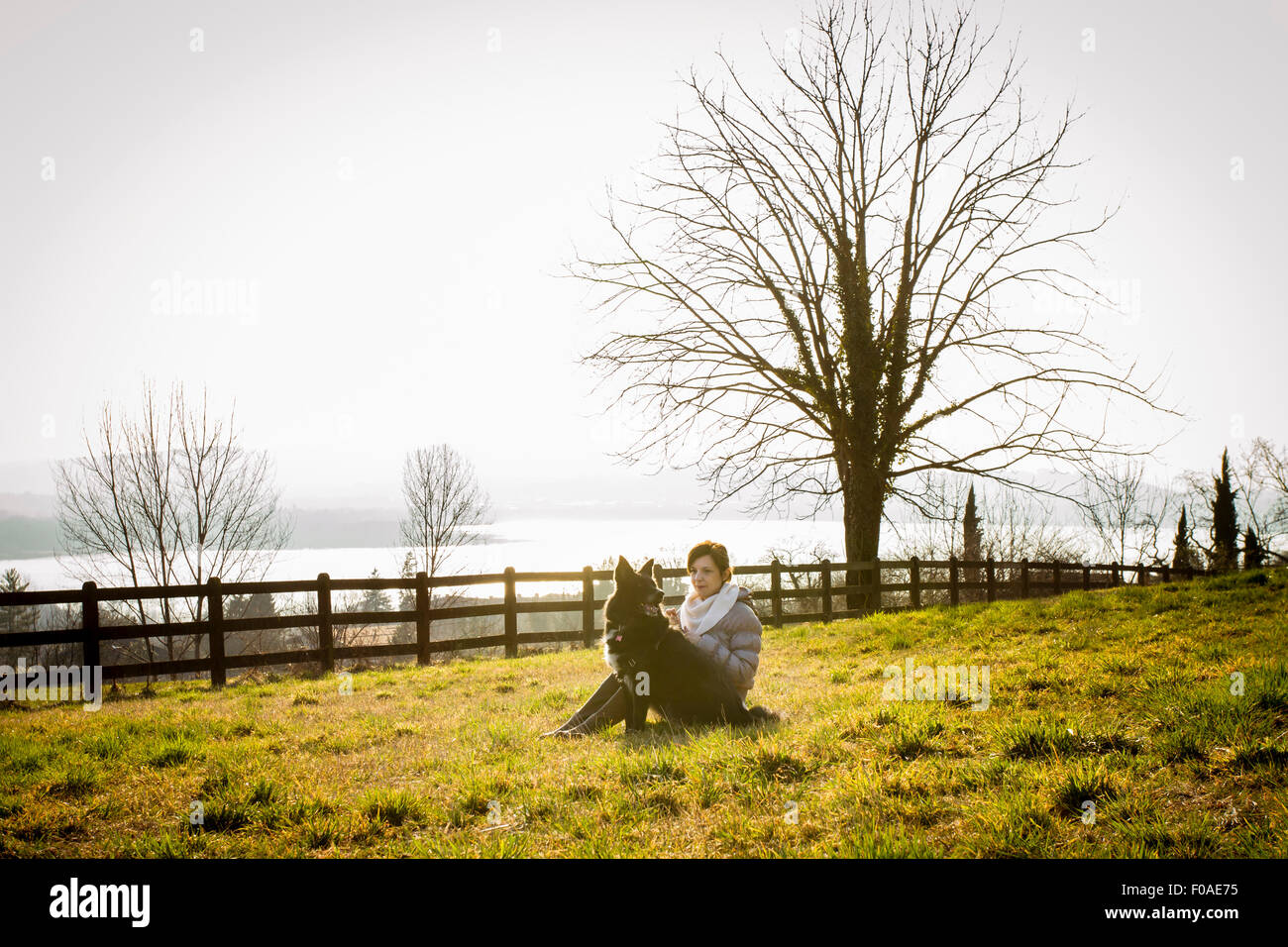 Metà donna adulta e il suo cane seduto in campo in riva al lago Foto Stock