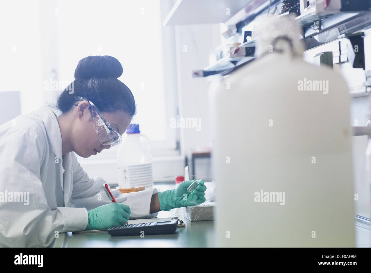 Giovane donna scienziato rendendo note di ricerca di laboratorio sul banco di lavoro Foto Stock