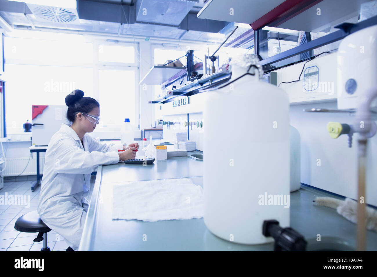 Giovane donna scienziato contemplando le note di ricerca sul banco di lavoro di laboratorio Foto Stock