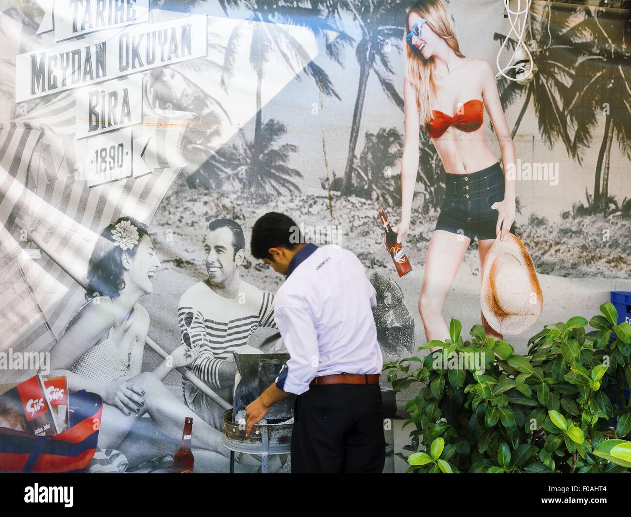 Uomo in piedi nella parte anteriore del ristorante pubblicizzato poster in Ataturk Caddesi, Izmir, Turchia Foto Stock