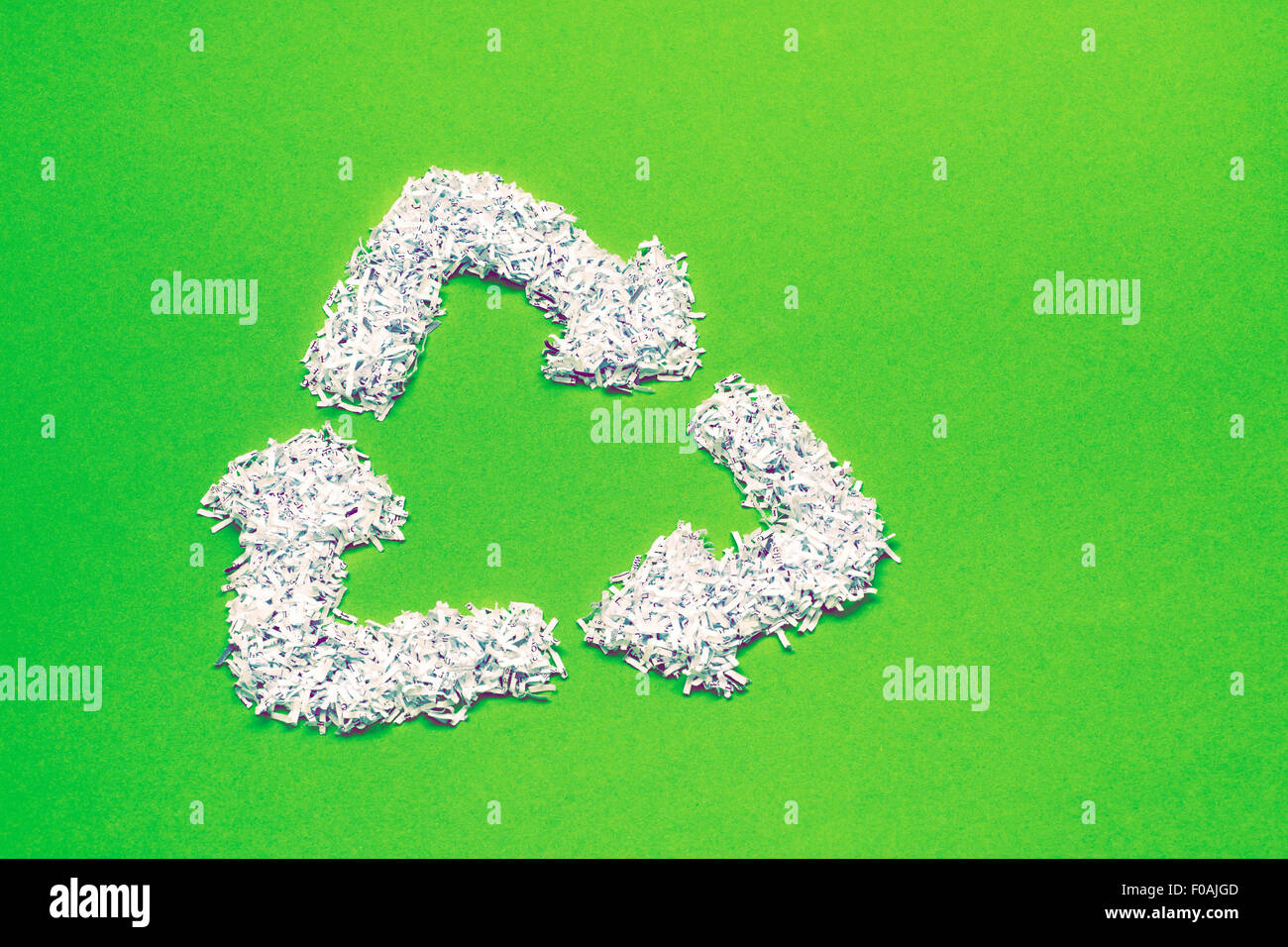 Simbolo di riciclaggio realizzato dal mucchio di shredded carta bianca brillante su sfondo verde Foto Stock