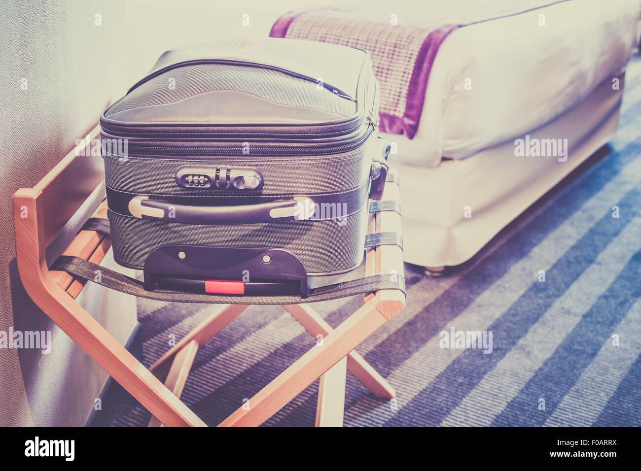 Camera in hotel con una valigia sul posto per i bagagli e il letto. Filtrata shot Foto Stock