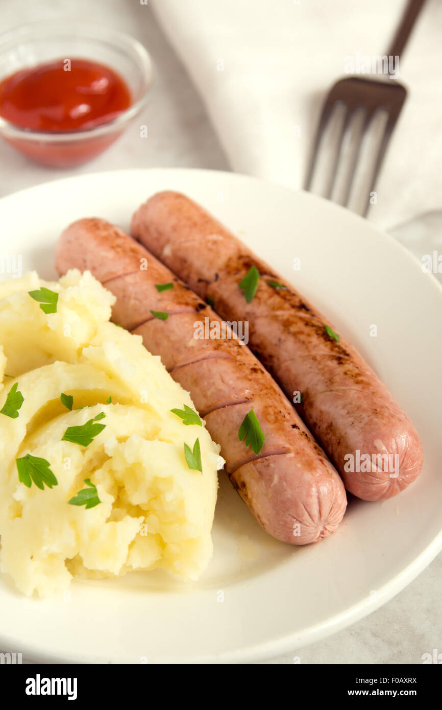 Purea di patate e salsicce con il prezzemolo e il ketchup sulla piastra bianca Foto Stock