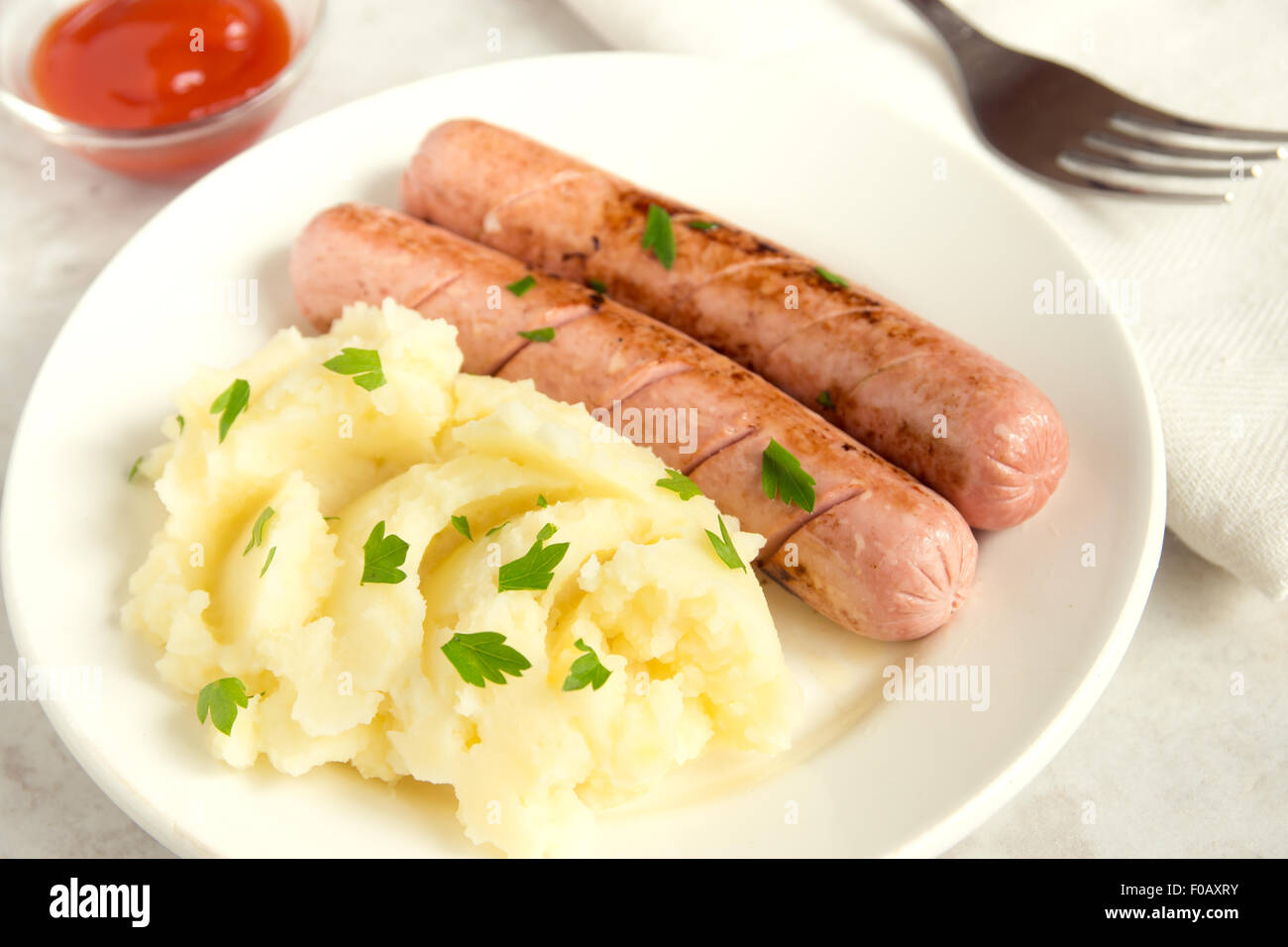 Purea di patate e salsicce con il prezzemolo e il ketchup sulla piastra bianca Foto Stock