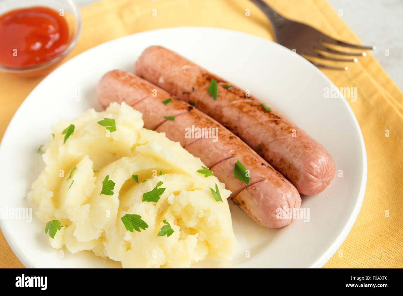 Purea di patate e salsicce con il prezzemolo e il ketchup sulla piastra bianca Foto Stock