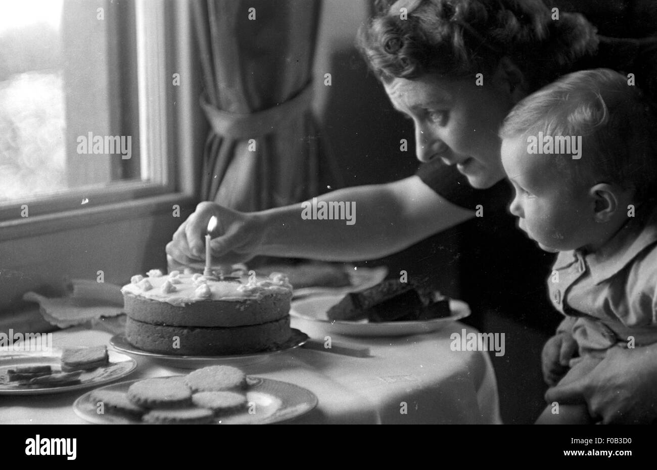 Una madre accendere una candela su una torta di compleanno per suo figlio Foto Stock