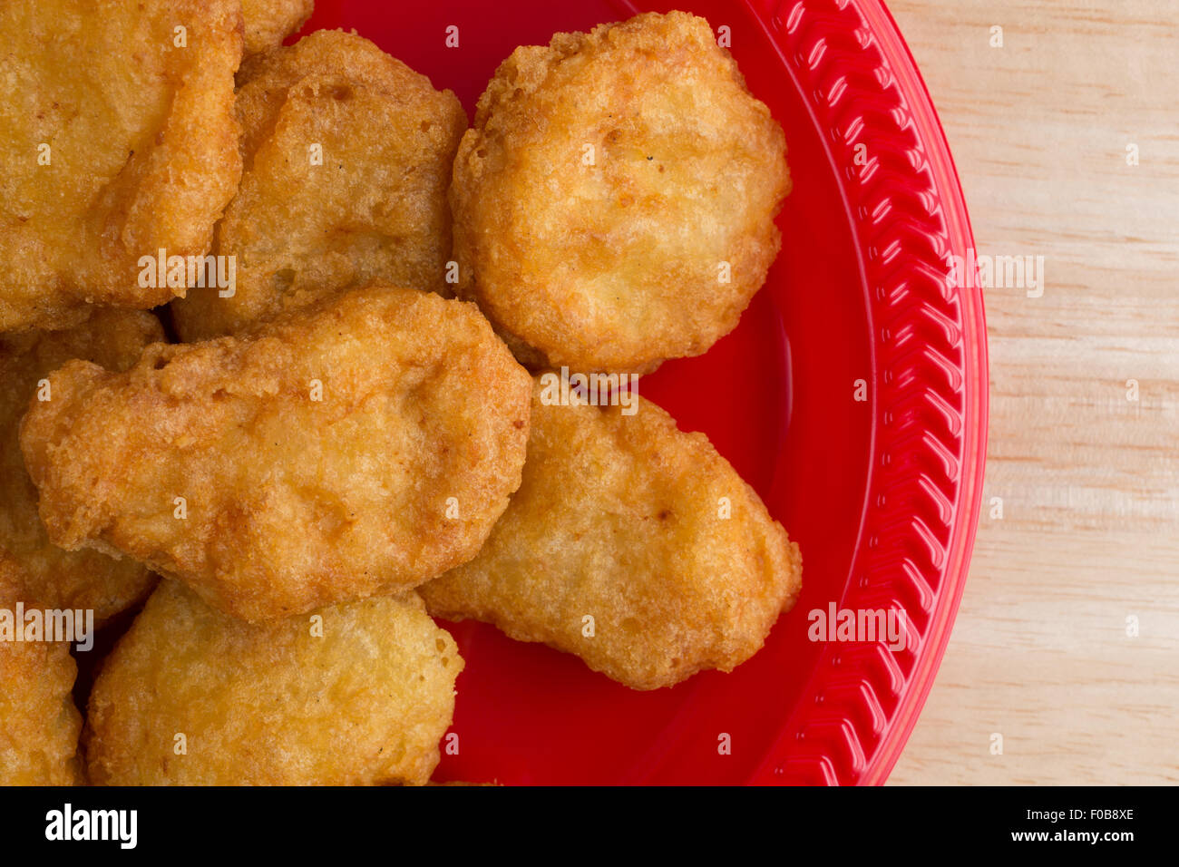 Top vista ravvicinata di un serving di pepite di pollo su una piastra di colore rosso su una tavola di legno top illuminato con luce della finestra. Foto Stock