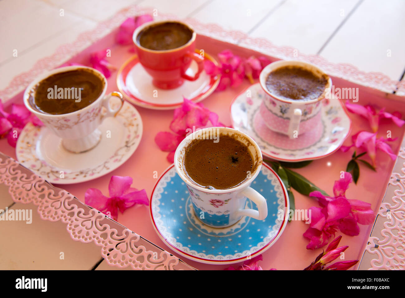 Quattro piccole coppe di schiumoso tradizionale caffè turco che serve in un colorato di rosa fiorito il vassoio sulla parte superiore di un bianco tavolo di legno in basso Foto Stock