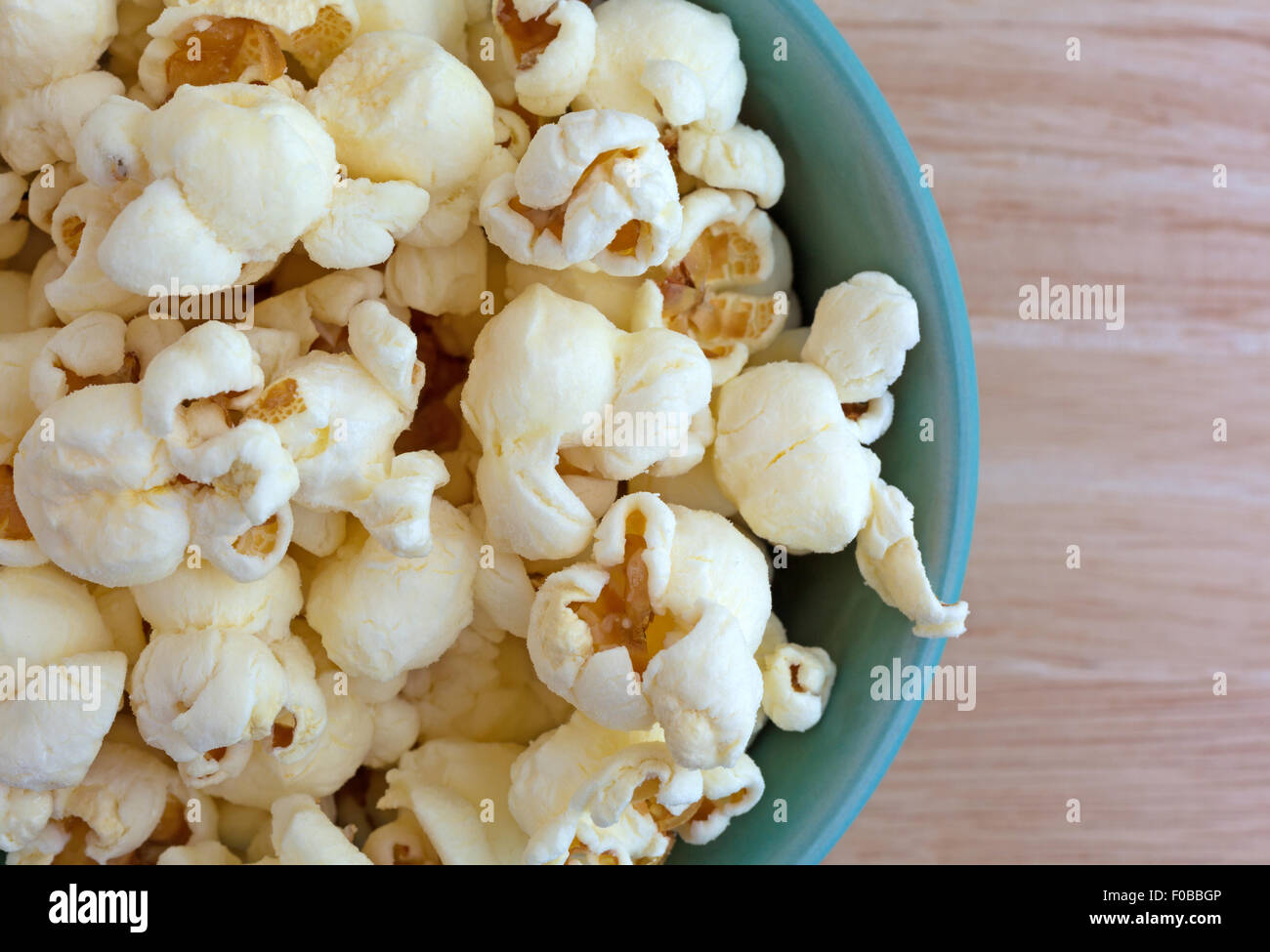 Top vista ravvicinata di una piccola ciotola riempita con una dose di formaggio cheddar bianco popcorn aromatizzato su una tavola di legno top Foto Stock