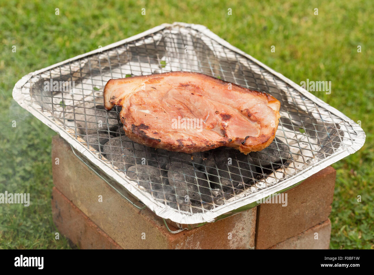 Un bacon essendo bistecca cotta su di un barbecue monouso all'aperto Foto Stock