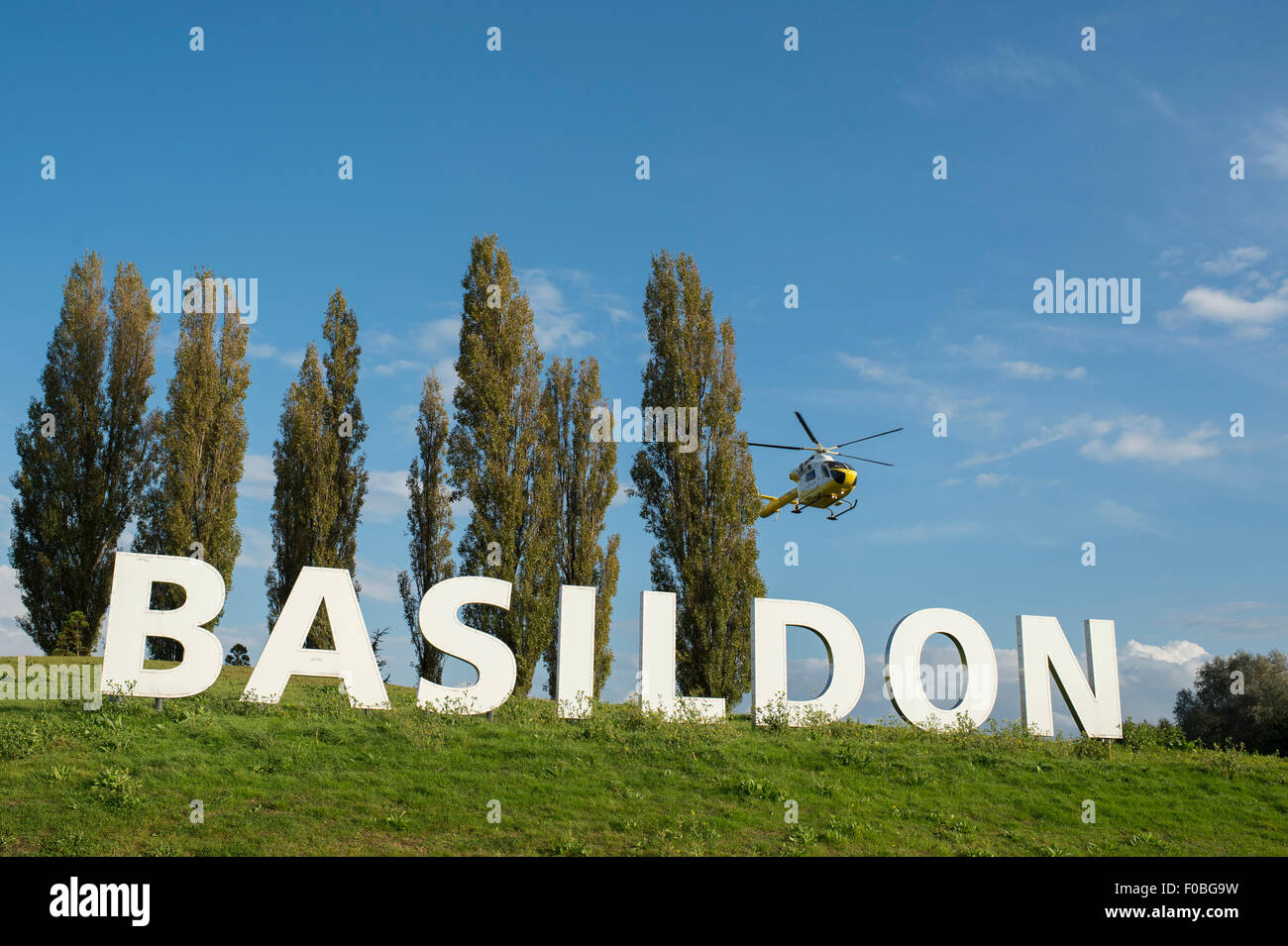 L'ora iconico segno di Basildon all'ingresso della città di Essex con la Herts ed Essex Air Ambulance sbarco accanto ad essa. Foto Stock