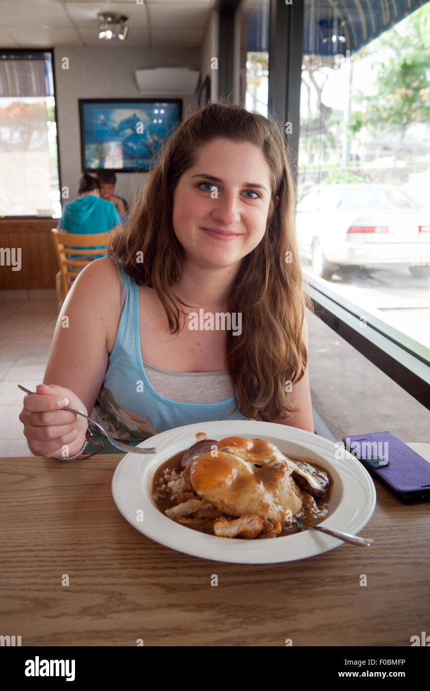 Una bella bruna ragazza gode di una loco moco, un popolare piatto hawaiano, a Big Island Grill, un ristorante in Kailua-Kona, Hawai'i. Foto Stock