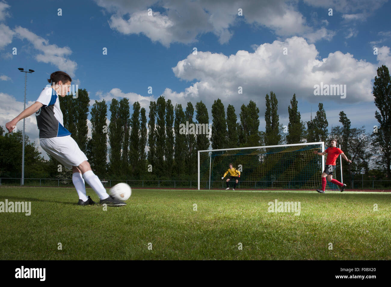 Per tutta la lunghezza della giovane giocatore di calcio calciare la palla verso la porta post Foto Stock