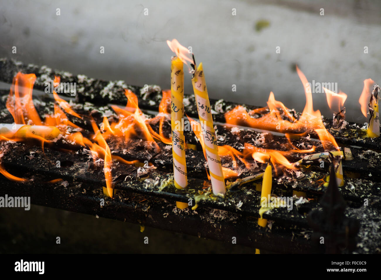 Cera residuo in fiamme intorno a due in giallo e bianco candele accese in un tempio buddista. Fino a fiamma per devozione Foto Stock