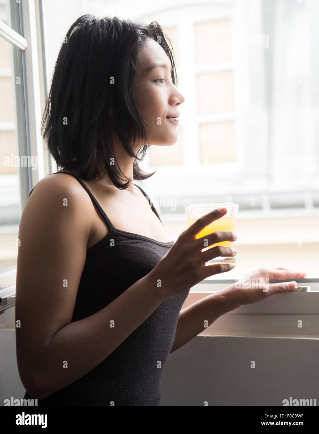 Giovane donna di fronte a una finestra aperta e bevande di succo d'arancia Foto Stock