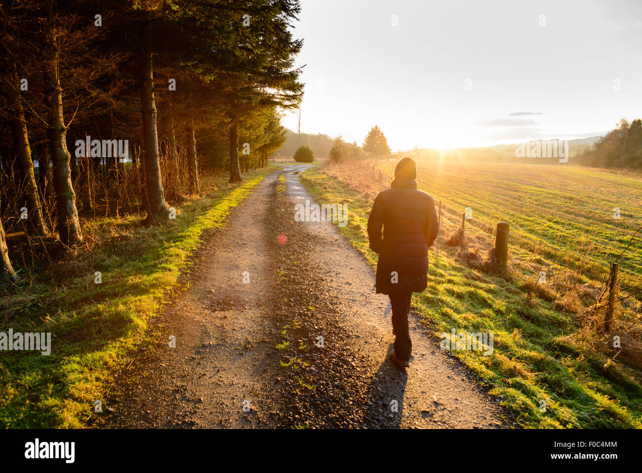 Una donna cammina lungo un cammino del paese verso il tramonto Foto Stock