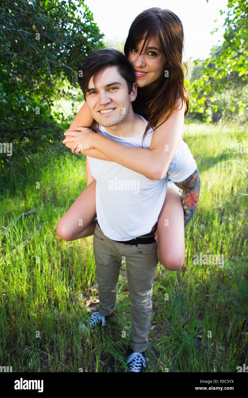 Giovane uomo dando ragazza piggyback ride in posizione di parcheggio Foto Stock