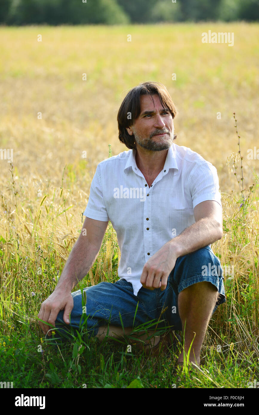 Un uomo si siede vicino a un campo di grano Foto Stock