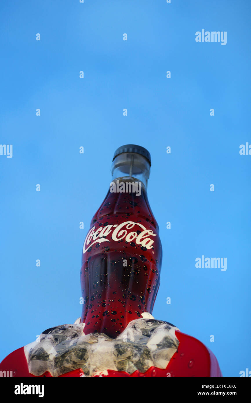 Illuminata coca cola bottiglia segno contro il cielo blu. Foto Stock