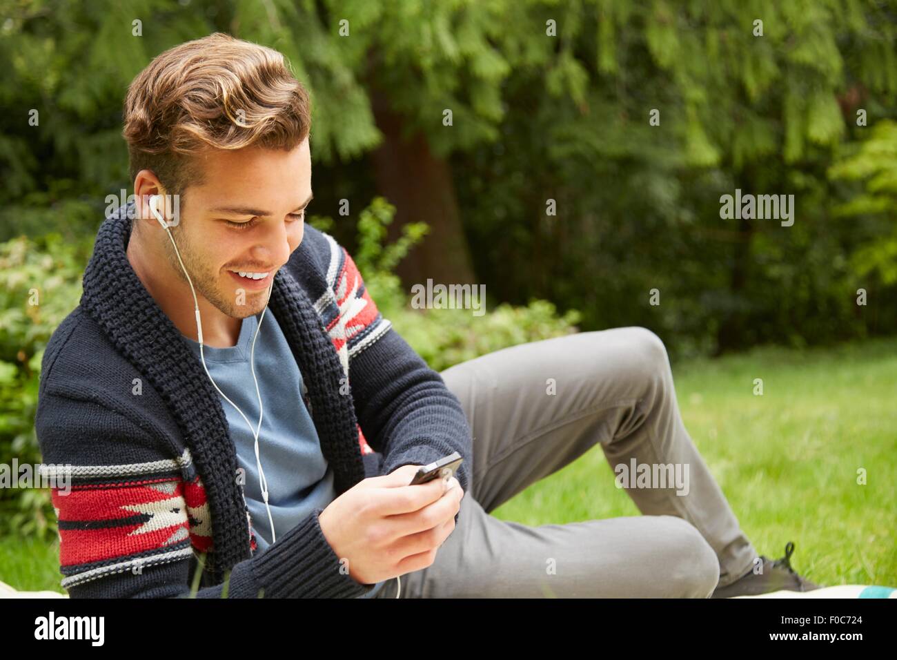Ritratto di uomo che stabilisce nel giardino di ascolto dello smartphone per indossare gli auricolari Foto Stock