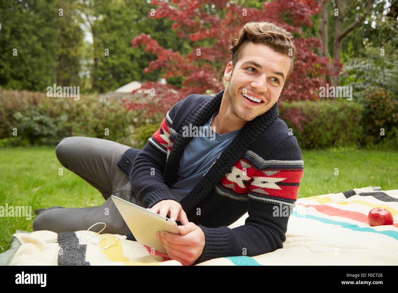 Ritratto di uomo sorridente posa in giardino la lettura digitale compressa Foto Stock