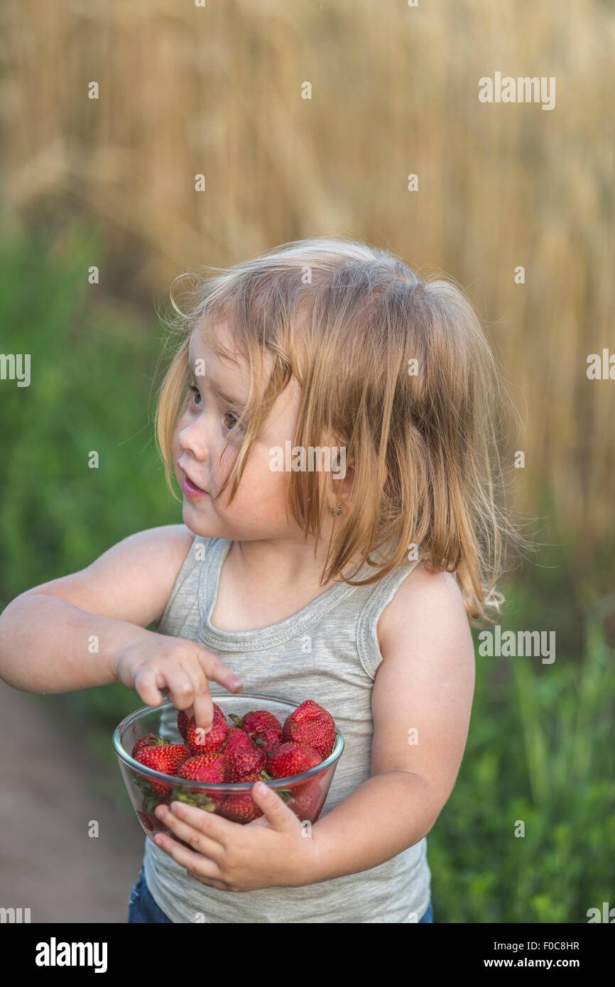 Carina ragazza con ciotola piena di fragole all'aperto Foto Stock
