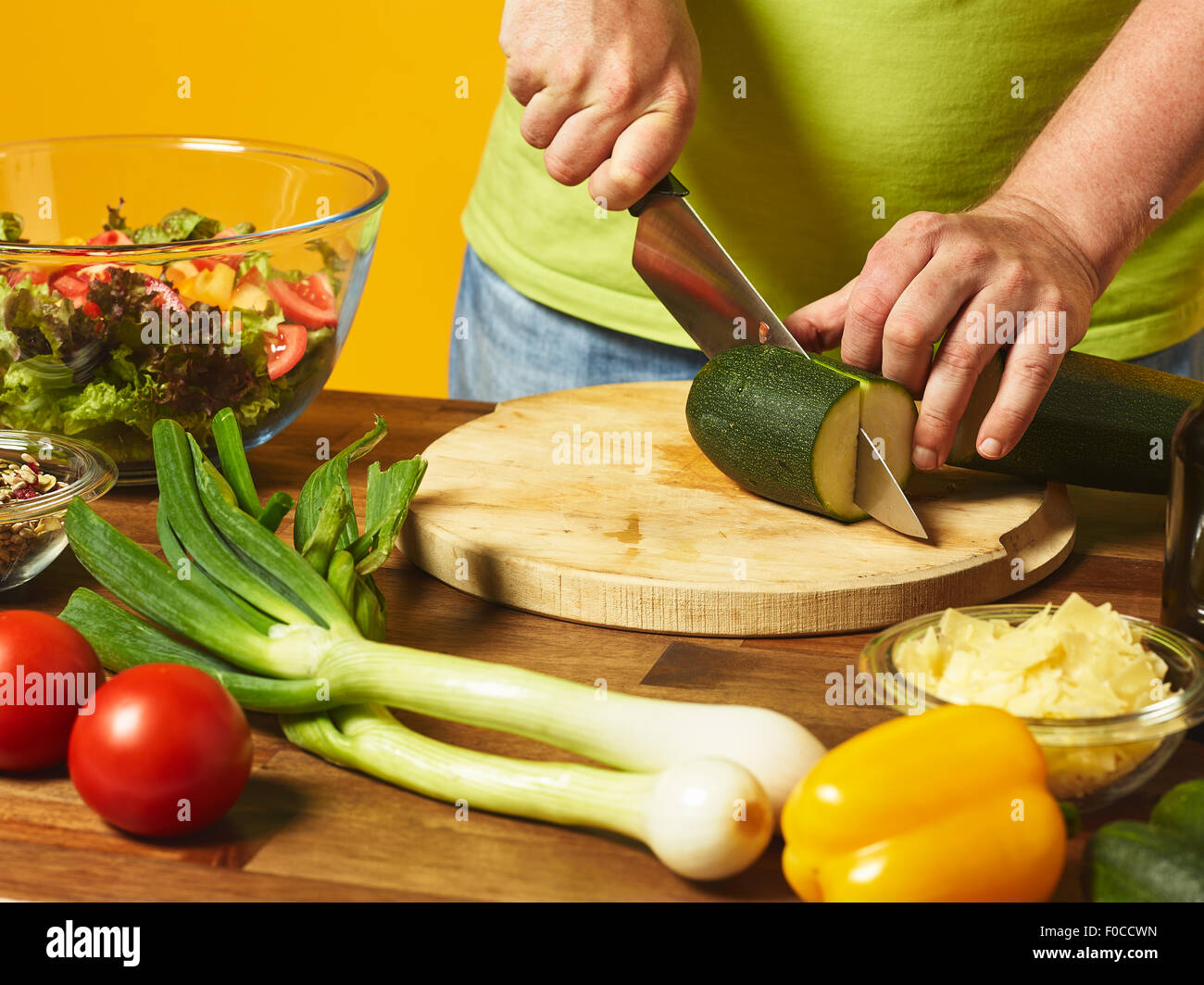 Insalata fresca ingredienti sul tavolo, uomo di mezza età taglia le zucchine - sfondo giallo Foto Stock