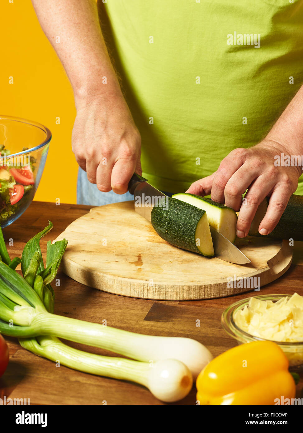 Insalata fresca ingredienti sul tavolo, uomo di mezza età taglia le zucchine - sfondo giallo Foto Stock