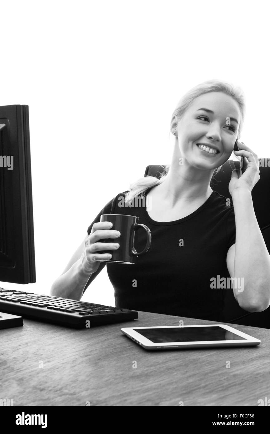 La donna posa alla sua scrivania di lavoro e parlando al telefono Foto Stock